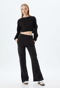 Zwarte cropped sweatshirt en high-waisted joggers, beide in een zachte stof. Opvallende details zijn de brede tailleband en de relaxed fit.