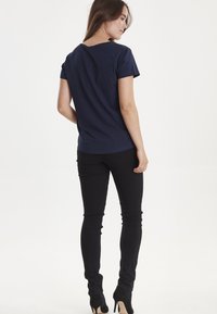 Mørkeblå kortærmet t-shirt med v-hals design, parret med sorte skinny jeans og sorte højhælede sko. Glat stofstruktur.
