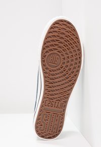 Semelle d'une chaussure de sport avec une bande de roulement en caoutchouc marron, motifs circulaires et croisillons, et texte en relief "H.I.S" et "NY1953".