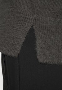 Mörkgrått stickat tröja med ribbad struktur, med en unik slits detalj vid nederkanten, kombinerat med svart tyg under.