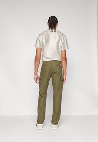 Green cargo pants with pockets, paired with a short-sleeved striped t-shirt. Person is facing away, standing against a neutral background.