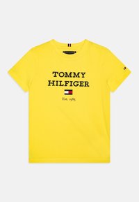 Żółta bawełniana koszulka z odważnym czarnym napisem "TOMMY HILFIGER" oraz "Est. 1985". Mała flaga logo na rękawie, design z okrągłym dekoltem.