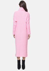 Langes, pinkes, geripptes Rollkragenkleid mit seitlichen Schlitzen, das lange Ärmel und eine lockere Passform hat. Getragen mit schwarzen Plateaustiefeln bis zum Knöchel.