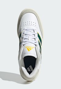 Bijele kožne tenisice s zelenim i žutim prugama, okrugli vrh, perforirani gornji dio i teksturirani suede akcent na peti. Adidas logo na jeziku.