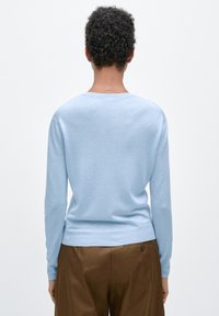 Lichtblauwe trui met een ronde hals en lange mouwen, gemaakt van een zachte gebreide stof. Glad oppervlak en aansluitend model.