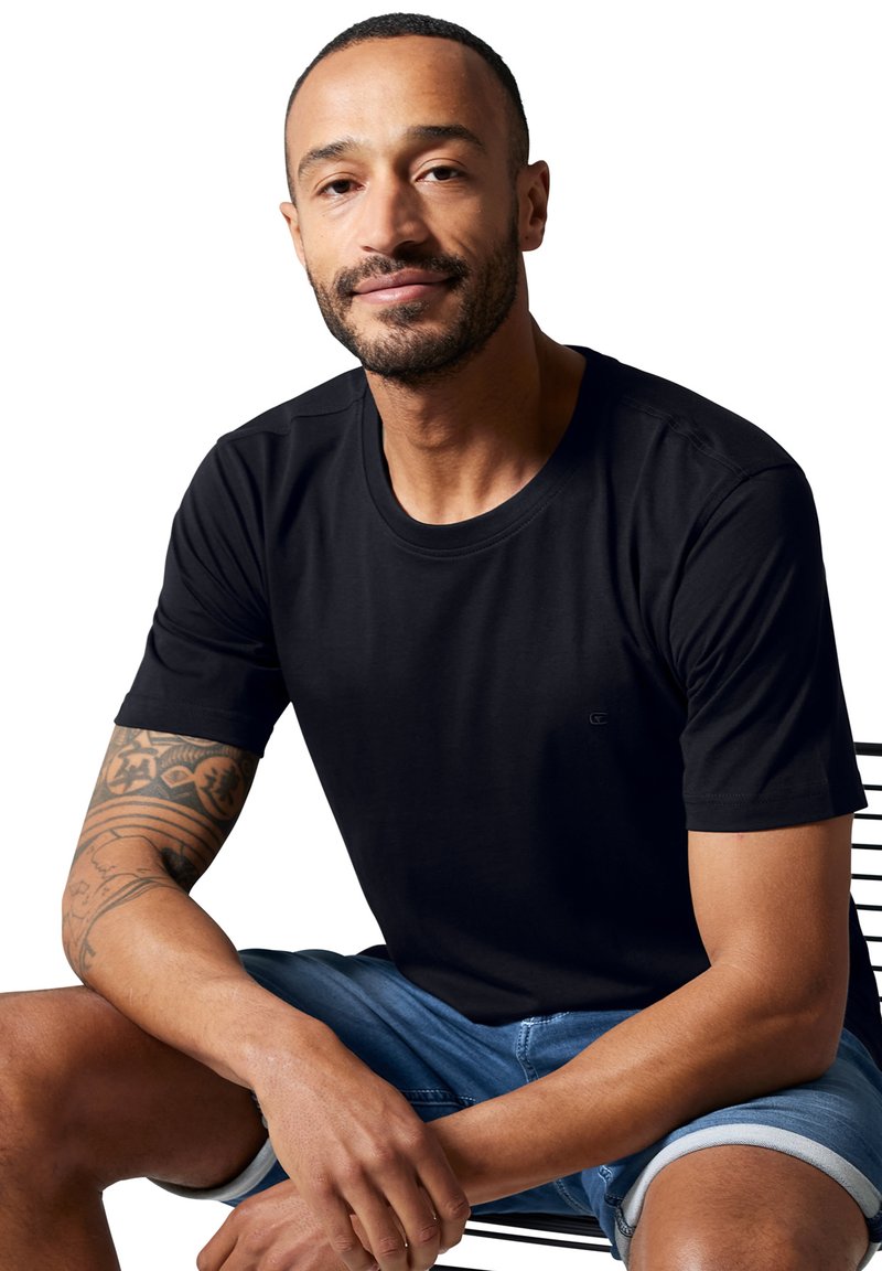 Sort kortærmet t-shirt med rund halsudskæring, lavet af glat stof, kombineret med denimshorts. Har et diskret logo på brystet.