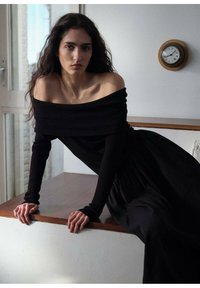 Čierny off-shoulder pruhovaný dlhý rukáv top skombinovaný s voľnou čiernou sukňou, umiestnený na neutrálnej pozadí s okrúhlym nástenným hodinami.