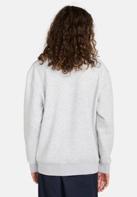 Grijze sweatshirt met een losse pasvorm, ribgebreide manchetten en onderrand, ronde hals en een zachte textuur. Van achteren zichtbaar met krullend haar.
