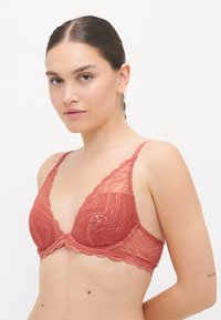 Mežģīņu apdare ar bralette siltajā terakotas krāsā, ar trīsstūrveida formu, caurspīdīgām krūštura krūšturiem un viļņainām malām. Regulējamas siksniņas pielāgošanai.