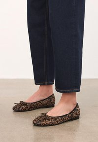 Lepardmönstrade ballerinas med svart kant, rundad tå och dekorativa rosetter, i kombination med mörk denim, cropped byxor.