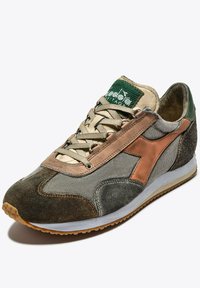 Zapatilla multicolor con una combinación de materiales en verde, beige y marrón. Presenta una parte superior de tela, acentos de cobre y una suela de goma.