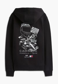 Svart hettejakke med hvitt motiv av racerbils hjelm, to Formel 1-biler, sjakkmønstret flagg, Cadillac-logo og teksten "Cadillac Formula 1 Team" på baksiden.