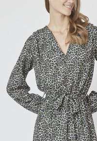 Leopardmønstret kjole i let stof med V-hals, lange ærmer og bælte i taljen. Farvepaletten inkluderer sort og beige.