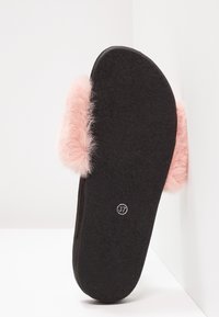 Mule noire avec une bride en fausse fourrure rose, semelle plate à fond texturé, taille 37 indiquée sur l'orteil. Design doux et confortable.