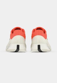 Αθλητικά παπούτσια με υφή στο ανοιχτό γκρι επάνω μέρος, πορτοκαλί λεπτομέρειες στη φτέρνα και λευκή ενδιάμεση σόλα. Διαθέτουν μαύρη καουτσούκ εξωτερική σόλα και στρογγυλεμένη σχεδίαση.