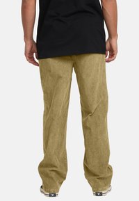Corduroy pants in a light tan color, featuring a loose fit and vertical ridges. Pair worn with a black t-shirt and sneakers.