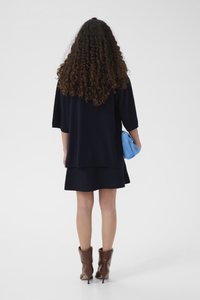 Pulover tricotat bleumarin cu mâneci scurte, asortat cu o fustă bleumarin și o geantă albastră. Modelul poartă cizme maro cu toc la gleznă. Păr texturat vizibil.