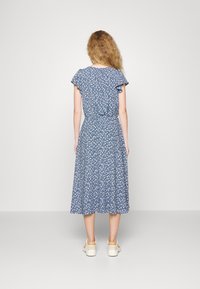 Blå blommig midiklänning med korta fladderärmar, figursydd midja och utställd kjol. Bärs med beigefärgade sneakers.