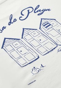 Trois cabines de plage aux contours bleus numérotées 21, 22 et 23 avec le texte « Casa de Playa » et deux petites silhouettes humaines en dessous sur un tissu blanc.