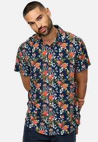 Camisa de manga corta, con botones, en navy con un estampado floral de flores rojas y rosas, hojas verdes y detalles blancos. Tejido de algodón, corte relajado.