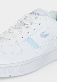 Λευκό sneaker Lacoste με ανοιχτό μπλε λεπτομέρειες, λευκά κορδόνια και το λογότυπο του κροκόδειλου Lacoste στη πλευρά και τη γλώσσα.