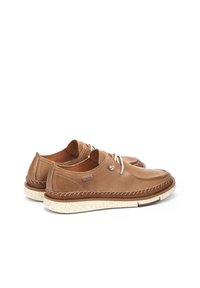 Zapatos de barco de cuero marrón con punta redonda, costuras blancas en contraste y una suela texturizada en crema. Presenta un diseño de cordones minimalista.
