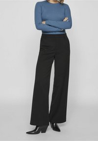 Pantalones de tiro ancho negros con un corte ajustado, que presentan una textura suave y sutiles bolsillos laterales, combinados con una blusa azul de manga larga ajustada.