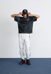 Sort grafisk oversized t-shirt med lyse mønstre, hvide tapered bukser med sorte striber og sort-røde træningssko.