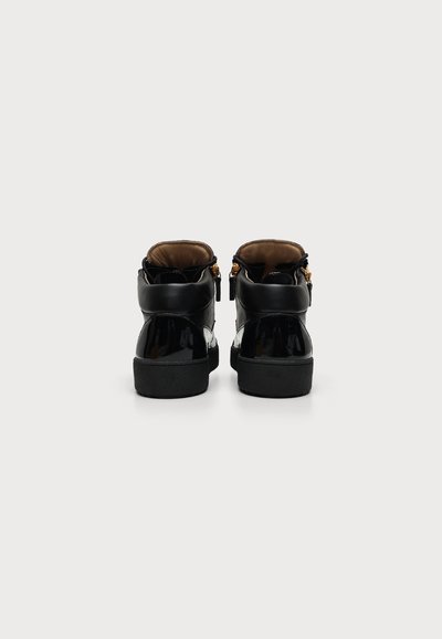 Ζευγάρι μαύρα sneakers με ψηλό πάνω μέρος και χρυσά φερμουάρ, εμφανίζονται από πίσω σε απλό λευκό φόντο.