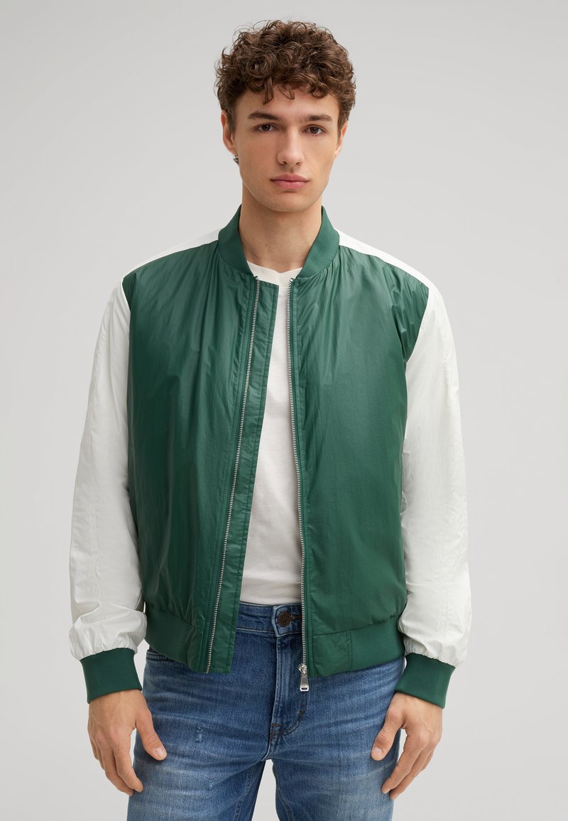 Giacca bomber verde e bianca con zip frontale, colletto e polsini a costine. Realizzata in materiali leggeri, presenta colori a contrasto sulle maniche.