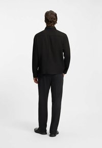 Chemise noire à manches longues avec un col à boutons, texture unie, coupe décontractée, associée à un pantalon noir côtelé et des chaussures plates noires.
