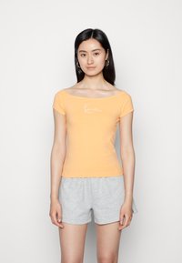 Πορτοκαλί εφαρμοστό t-shirt με κοντά μανίκια, φαρδιά λαιμόκοψη και λευκή υπογραφή εκτύπωσης. Συνδυάζεται με γκρι σορτς. Λείο βαμβακερό ύφασμα.