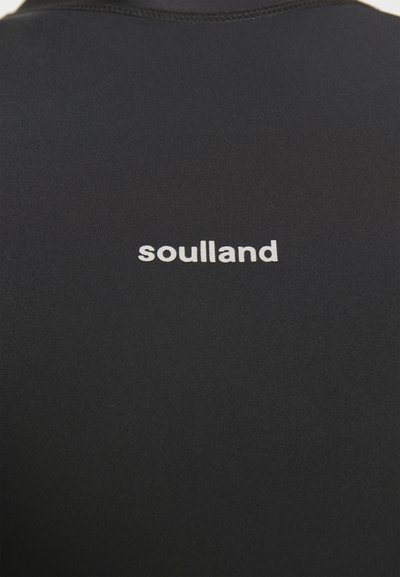 Svart tettsittende skjorte laget av glatt stoff, med ordet "soulland" i små hvite bokstaver på den øvre ryggen.