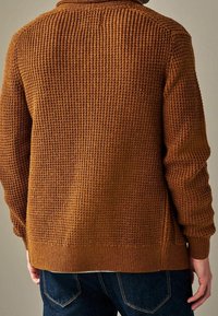 Cardigan marrone lavorato a maglia con un motivo testurizzato, polsini e orlo a coste. La vista posteriore mostra una vestibilità rilassata e dettagli minimi. Jeans in denim visibili.