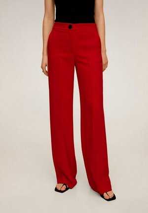 Mujer con pantalones rojos de tiro alto y pierna ancha, combinados con top negro sin mangas y sandalias negras abiertas, sobre un fondo claro.