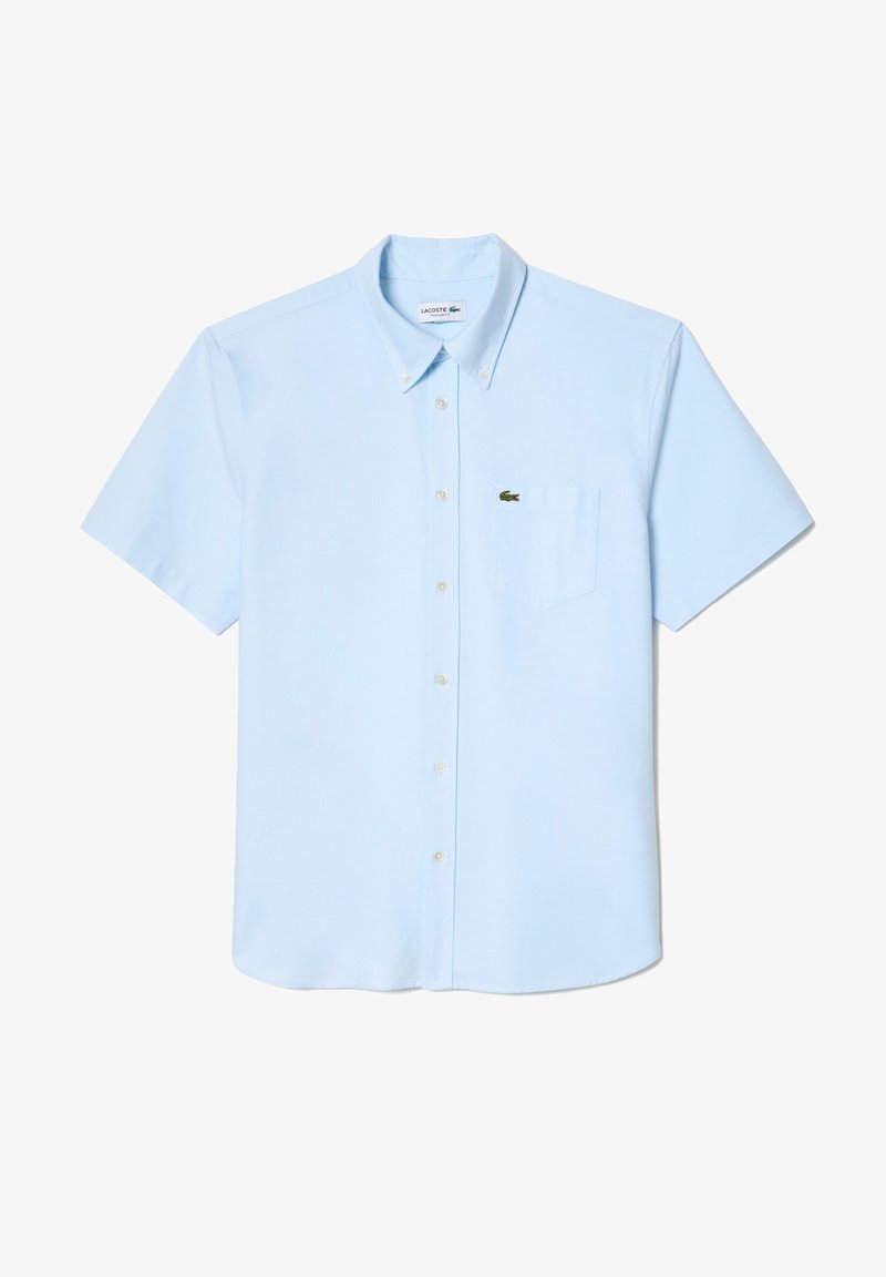Chemise à manches courtes bleu clair en coton, munie d'un col et d'une poche poitrine gauche arborant un petit logo de crocodile vert.