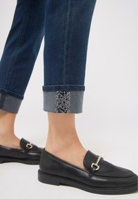 Mustad nahast loafers kuldse accenti bucklega, kombineeritud tumedate teksapükstega, millel on keeratud serv ja hõbedased sädelused hemmi ääres.