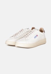 Sneaker in pelle bianca con accenti beige, lacci piatti e una suola in gomma testurizzata. Presenta un upper cucito e un piccolo logo sul lato.