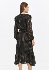 Czarna sukienka w kropki z złotymi punktami, przejrzysta tkanina, falbany na rękawach, dopasowana talia i warstwowy dół.