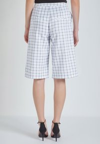 Pantalones cortos blancos a cuadros con patrón de cuadrícula en azul marino, de longitud a la mitad del muslo, con una textura suave y cuatro bolsillos traseros.