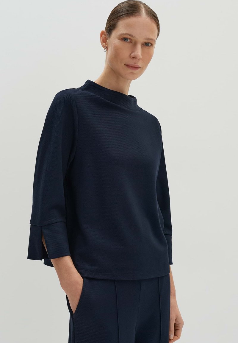 Pull bleu marine à col montant, à manches trois-quarts et avec des fentes latérales. Fabriqué en tissu texturé, présentant une coupe décontractée.