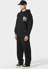 Musta puuvillapaita, jossa on etutasku ja värikäs kukkakuva rinnassa. Yhdistetty löysiin mustiin housuihin ja lenkkareihin.