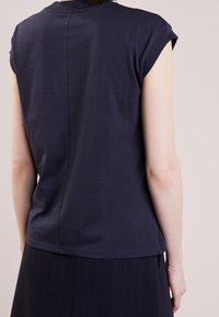 Námořnická modrá bavlněná tričko s krátkými rukávy, bezešvé provedení zad a hladká textura. V kombinaci s tmavě pruhovanou sukní.