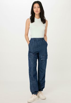 Denim-Cargo-Hosen mit elastischem Bund, Seitentaschen und schmal zulaufenden Knöcheln; kombiniert mit einem enganliegenden, hellgrünen ärmellosen Oberteil.