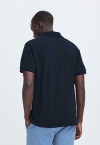 Polo à manches courtes en tissu uni bleu marine. Doté d'un col, d'épaules structurées et d'une coupe décontractée avec un ourlet droit.