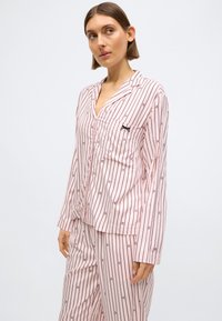 Set de pijama roz cu dungi, confecționat dintr-un material moale, cu mâneci lungi, nasturi în față și buzunar pe piept cu un mic detaliu negru.