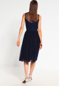Abito blu navy con schiena trasparente a pois, corpetto aderente e gonna di tulle fluida che arriva sotto il ginocchio. Tacchi argentati completano il look.