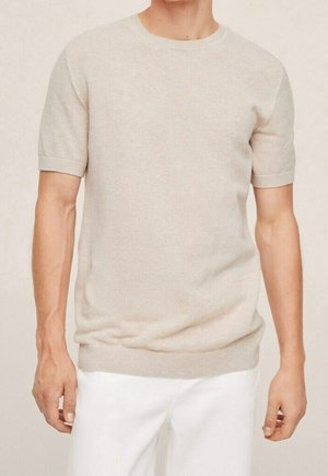 Beżowy sweter z krótkim rękawem, o okrągłym dekolcie, z fakturowanej dzianiny, dopasowanym kroju, zestawiony z białymi spodniami.