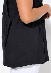 Top in cotone nero con pizzo lungo i lati, caratterizzato da un colletto rotondo e una vestibilità ampia. Il tessuto appare liscio e morbido.