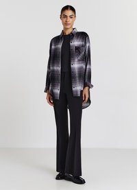 Camicia a quadri nera, grigia e bianca, con taschino sul petto decorato. Indossata su una maglietta nera e abbinata a pantaloni svasati.